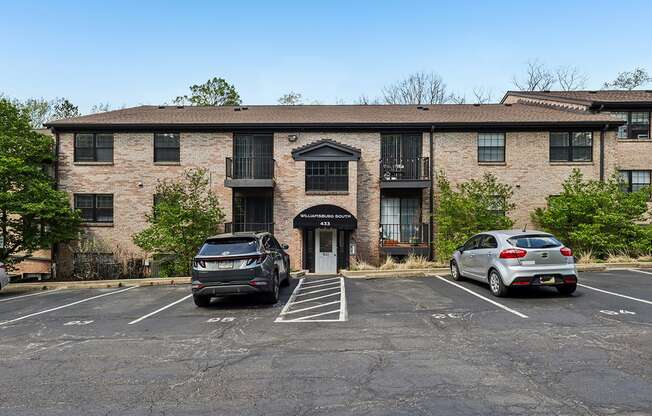 A parking lot in front of a brick building with two cars parked.