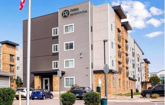 a building with a flag and cars parked in front of it at Parks Residential - Denver, Centennial, CO 80111
