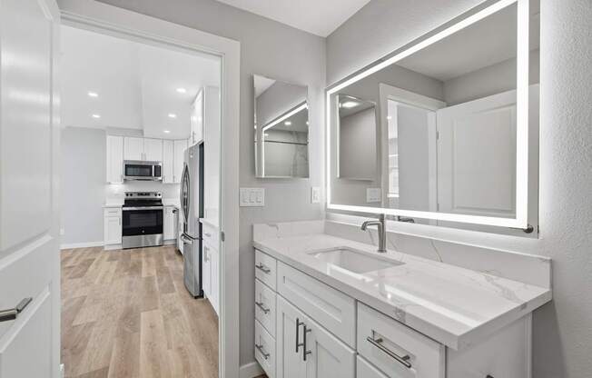 A modern kitchen with a white countertop and a large mirror above the sink.