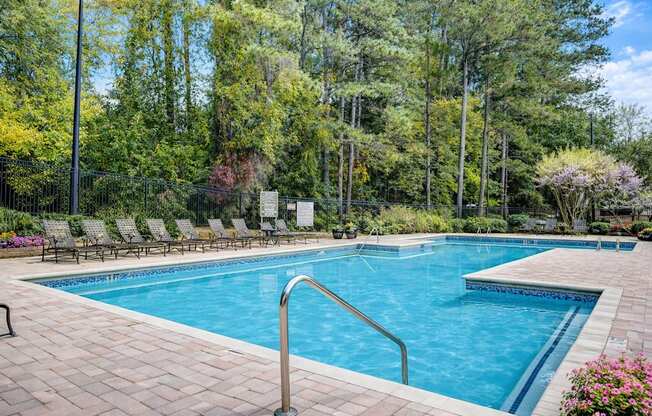 A large swimming pool surrounded by trees and chairs.