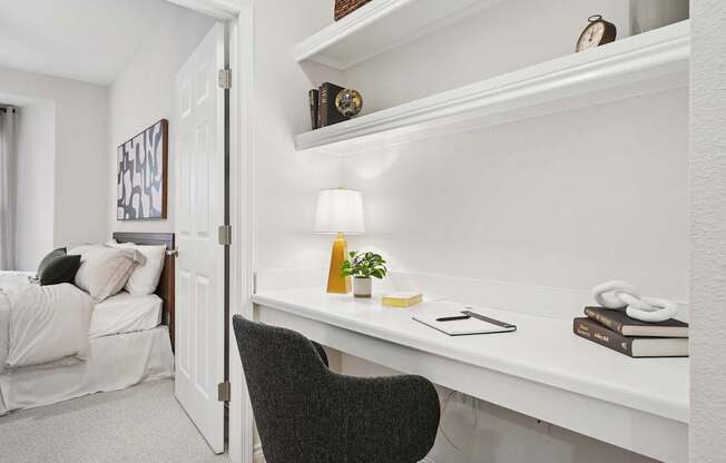 A white desk with a black chair and a lamp on it.