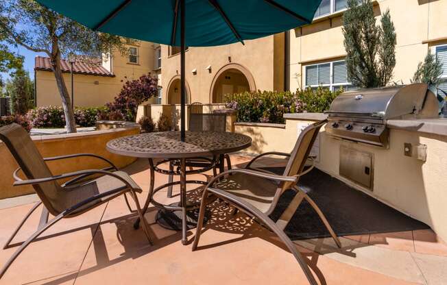 a patio with a grill and a table with chairs and an umbrella