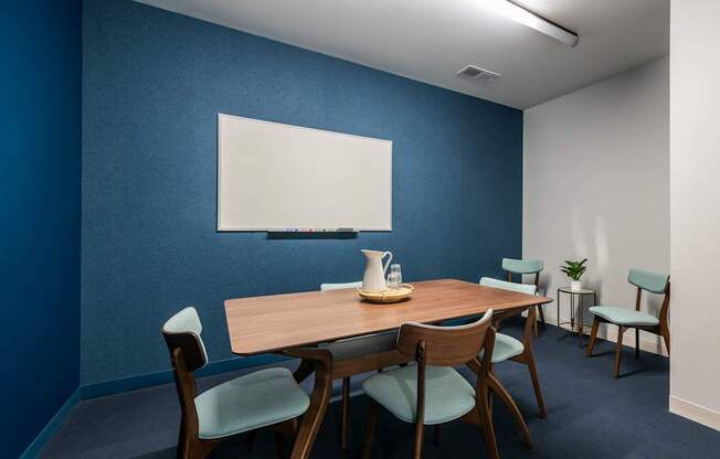 a conference room with a table and chairs and a whiteboard on a blue wall
