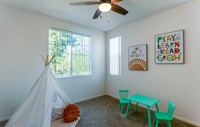 A room with a teepee, a table and chairs, and two posters on the wall.