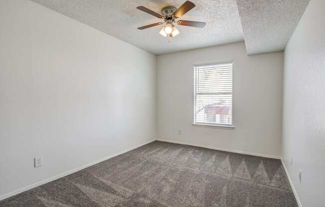 an empty living room with a ceiling fan and a window