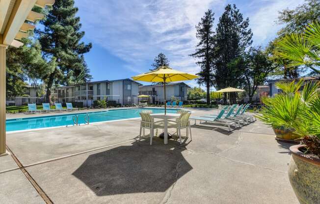 Community swimming pool area with tables, chairs and umbrellas for shade. at Renaissance Park Apartments, Davis, California