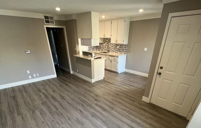 View into living area, dining area, and kitchen. Has recessed lighting, wood like flooring, and white cabinets.