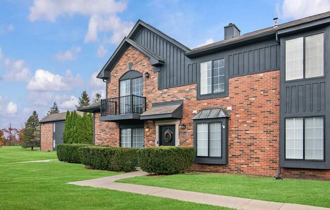 A red brick house with a balcony and a green lawn in front.