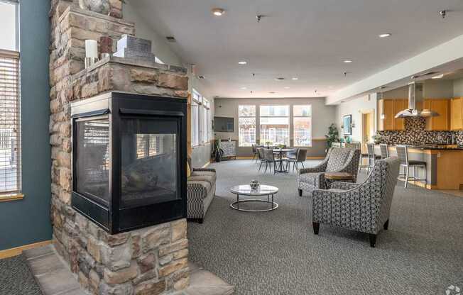 A stone fireplace is in the corner of a room with grey carpeting.