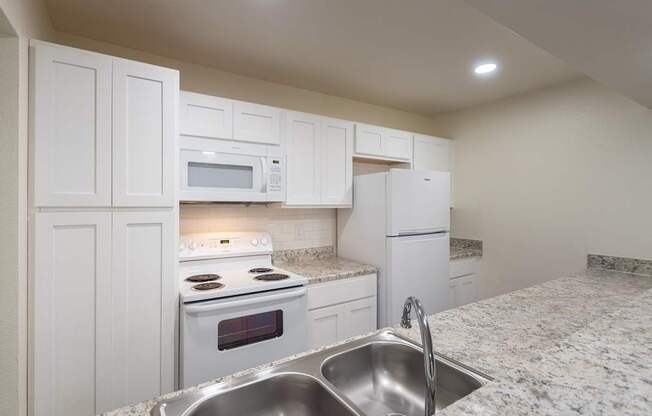 A kitchen with white appliances and cabinets with hardwoodlike flooring throughout in a 2 bedroom, 2 bath 991 sq ft apartment home at The Biltmore Apartments located in the Vickery Midtown neighborhood of Dallas, TX.