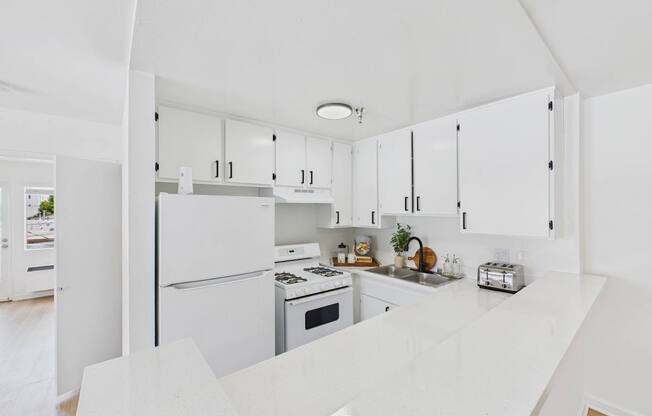 A white kitchen with a refrigerator, oven, and sink.