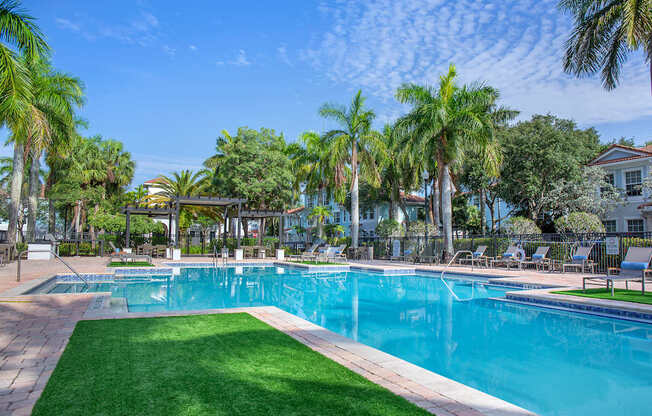A large swimming pool surrounded by palm trees and lounge chairs at Floresta apartments in Jupiter, FL