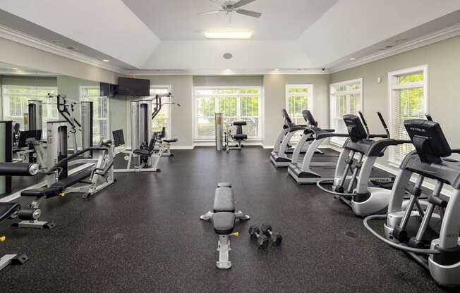 A spacious gym with various exercise machines and a ceiling fan.