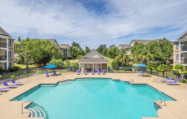 A large swimming pool surrounded by purple lounge chairs and a gazebo.