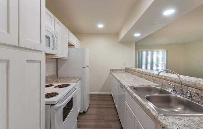 A kitchen with white appliances and cabinets with hardwoodlike flooring throughout in a 2 bedroom, 2 bath 991 sq ft apartment home at The Biltmore Apartments located in the Vickery Midtown neighborhood of Dallas, TX.