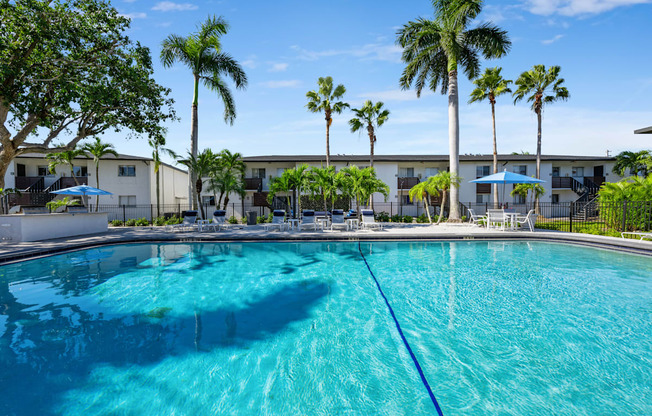 a large swimming pool with palm trees and a building in the background
