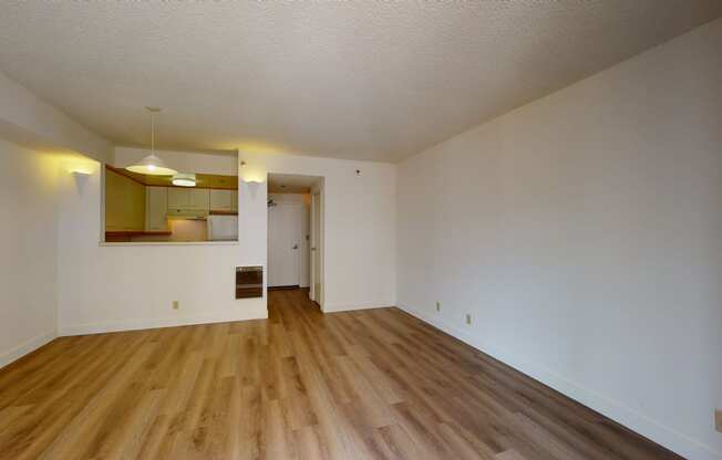 an empty living room with hardwood floors and a kitchen in the background