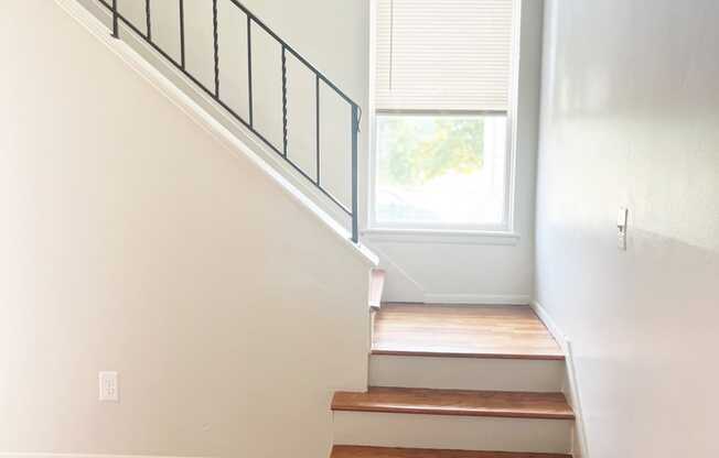 A photo of a bright staircase with a window and a black railing.