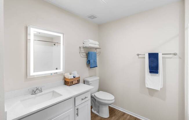 A white bathroom with a toilet, sink, mirror, and towel rack.