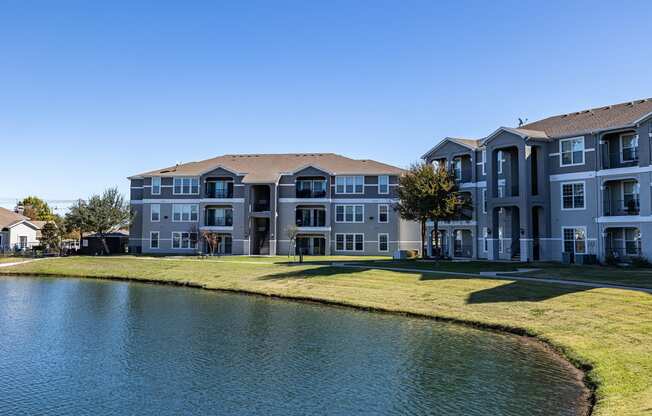 an apartment building overlooks a pond in front of a grass field