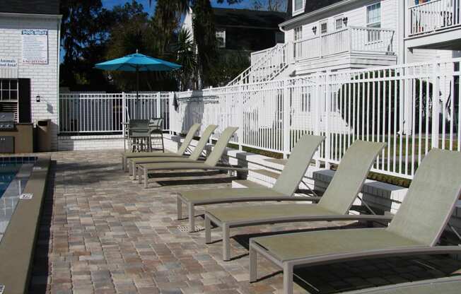 a row of chaise lounges on a brick patio next to a pool