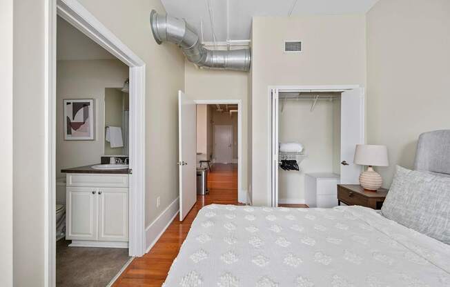 A bedroom with a bed, nightstand, and a small kitchen area.