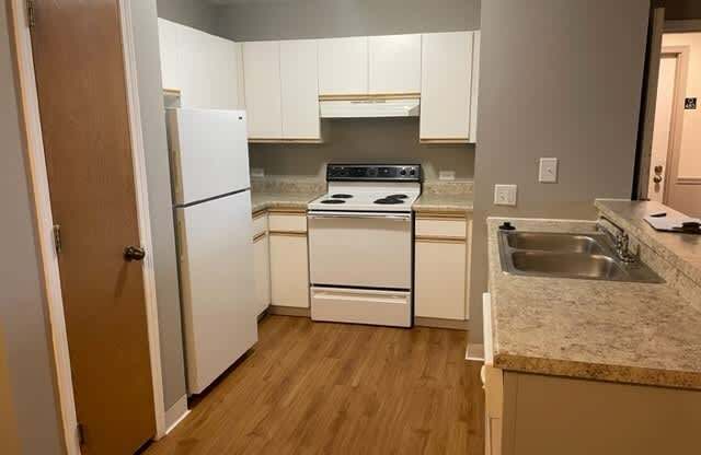 A kitchen with white appliances and wooden floors.
