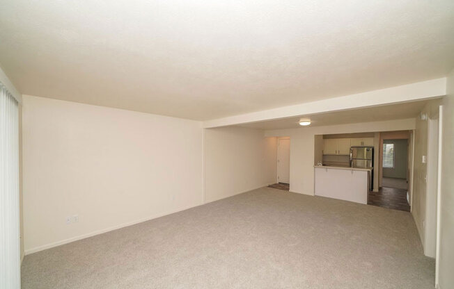 an empty living room with a kitchen in the background