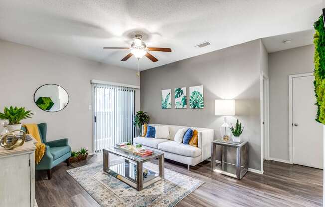 A living room with a white couch, a glass coffee table, and a ceiling fan.