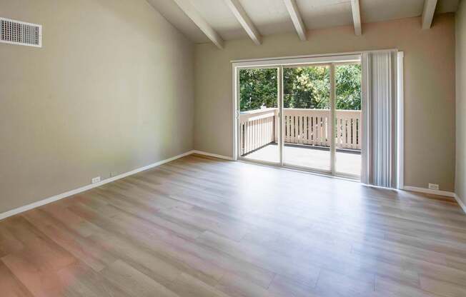 A room with wooden flooring and a sliding glass door leading to a balcony.