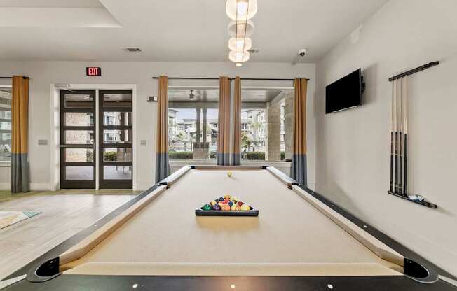 A pool table with a TV mounted on the wall and a fireplace in the background.
