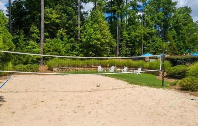 A sandy volleyball court surrounded by trees and a fence.