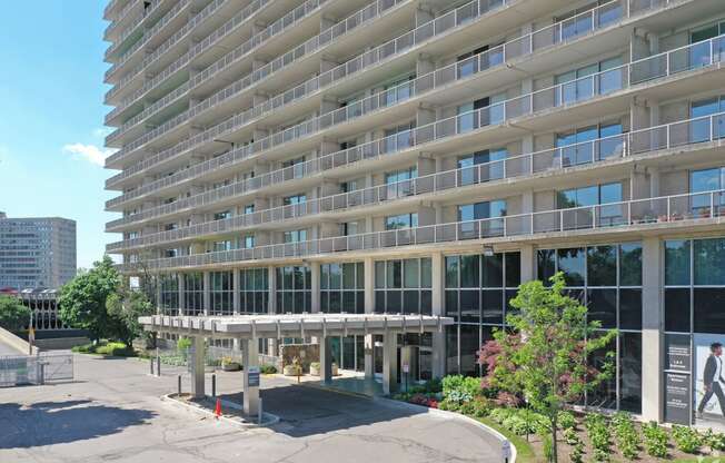 Exterior of the Jefferson. The image shows the parking lot and main enterance to the building. The building stands 30 stories tall. There is green flowers around the outside of the building.