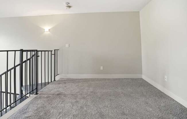 A spacious room with a carpeted floor and a staircase with black railings.