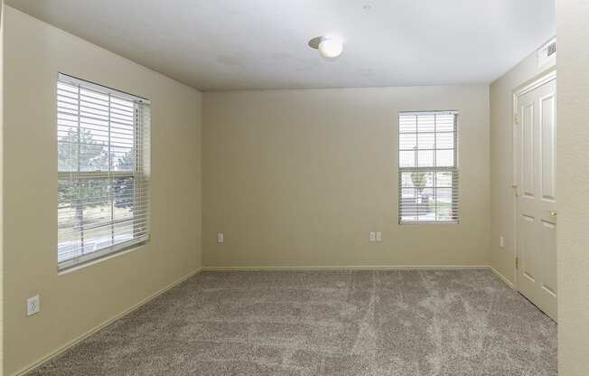 A room with a carpeted floor, two windows, and a door.