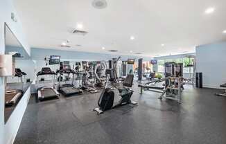a spacious fitness room with cardio equipment and flat screen tvs
