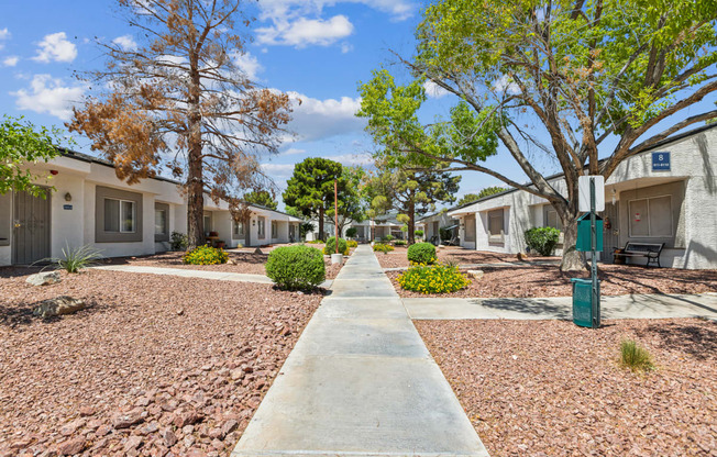 an empty sidewalk between two buildings with trees and plants