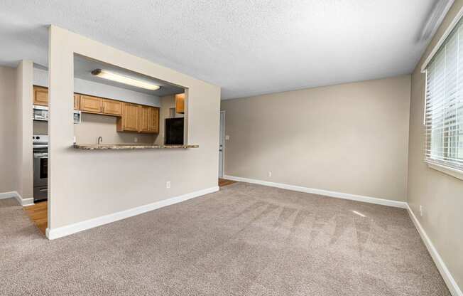 an empty living room with a kitchen in the background