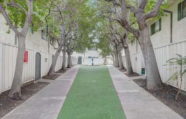 a green walkway between two white buildings with trees