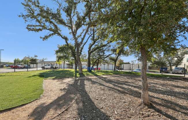 a park with trees and grass near a parking lot