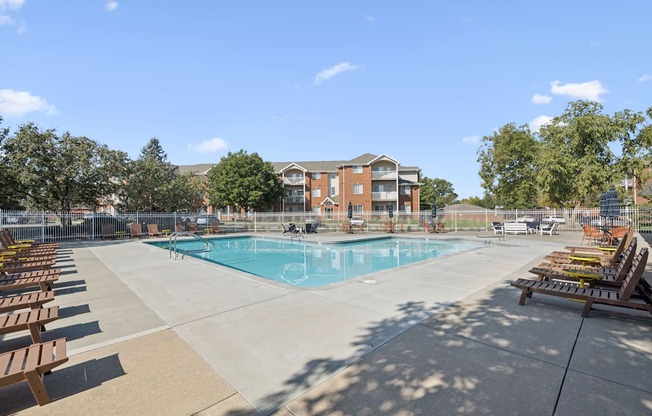 A large swimming pool surrounded by sun loungers and trees.