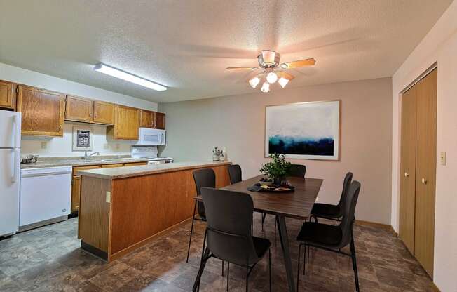 a dining area with a table and chairs and a kitchen in the background. Fargo, ND Kennedy Apartments