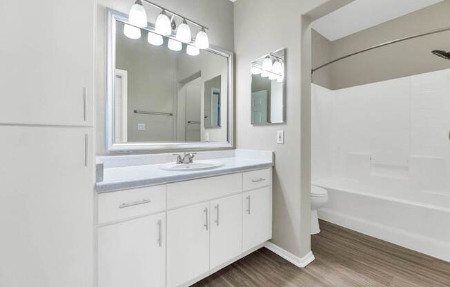 A white bathroom with a sink, mirror, and wooden floors.