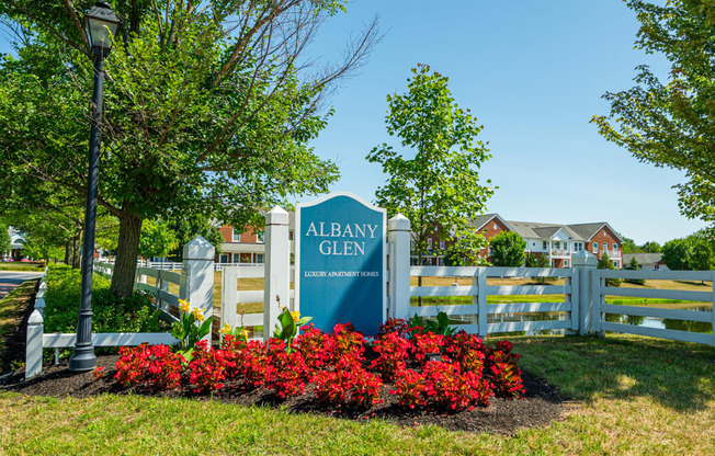 a sign for albany glen in front of a fence and red flowers