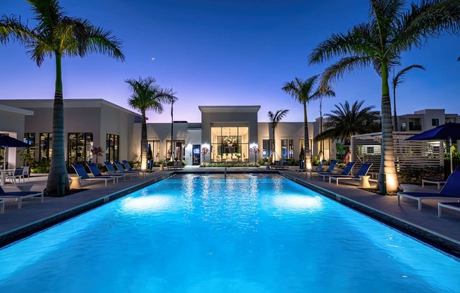 A swimming pool in front of a building with palm trees.