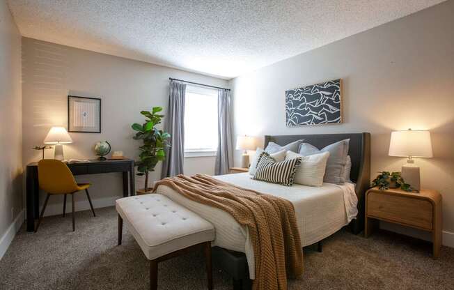 A bedroom with a bed, desk, chair, and two lamps.