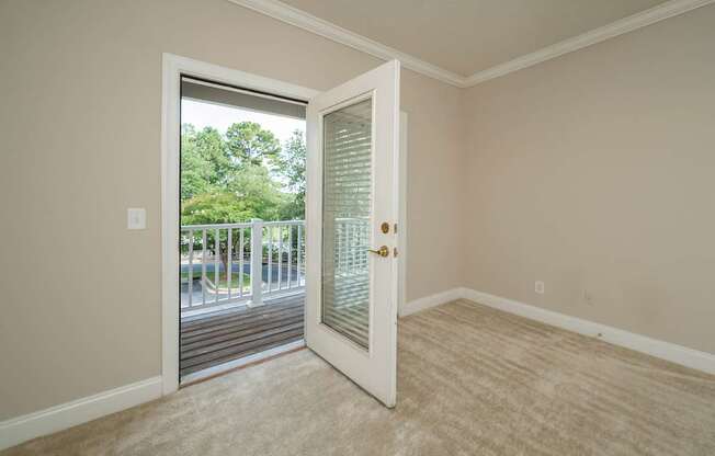 A room with a white door and a window showing a view of trees and a parking lot.