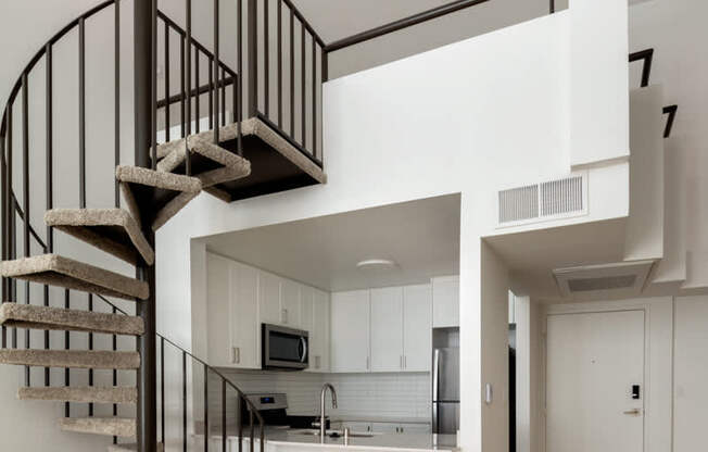 A spiral staircase with a metal railing and wooden steps leads to a kitchen area.