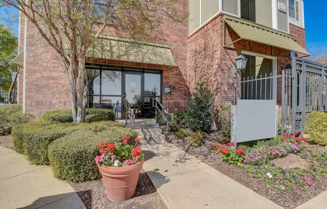 a sidewalk in front of a brick building with flowers and bushes