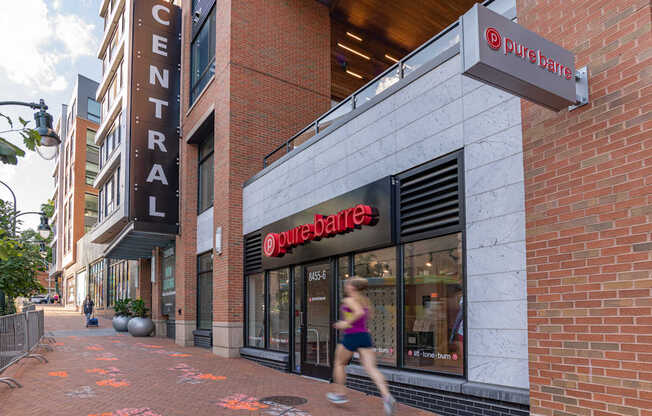 A woman runs past a Pure Barre studio on a city sidewalk.